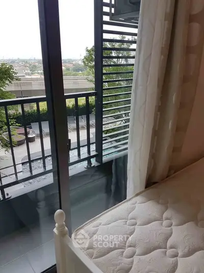 Cozy bedroom with balcony view overlooking lush greenery and urban landscape.