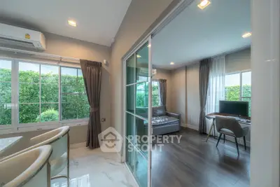 Modern living room with large windows and stylish decor, featuring a cozy seating area and a work desk.