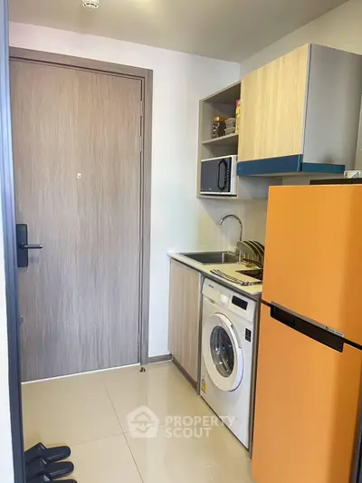 Compact kitchen with vibrant orange fridge and washing machine in modern apartment