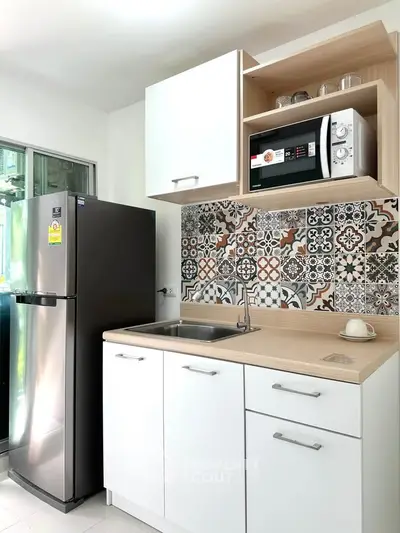 Modern kitchen with stylish backsplash, stainless steel fridge, and microwave in compact layout.