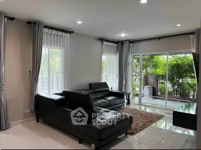 Spacious living room with modern black leather sofas and large windows opening to a lush balcony view.