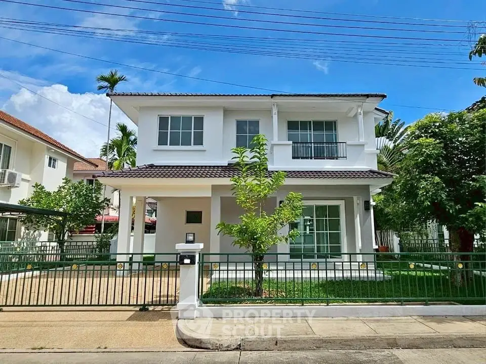 Charming two-story white house with lush green garden and gated driveway in suburban setting.