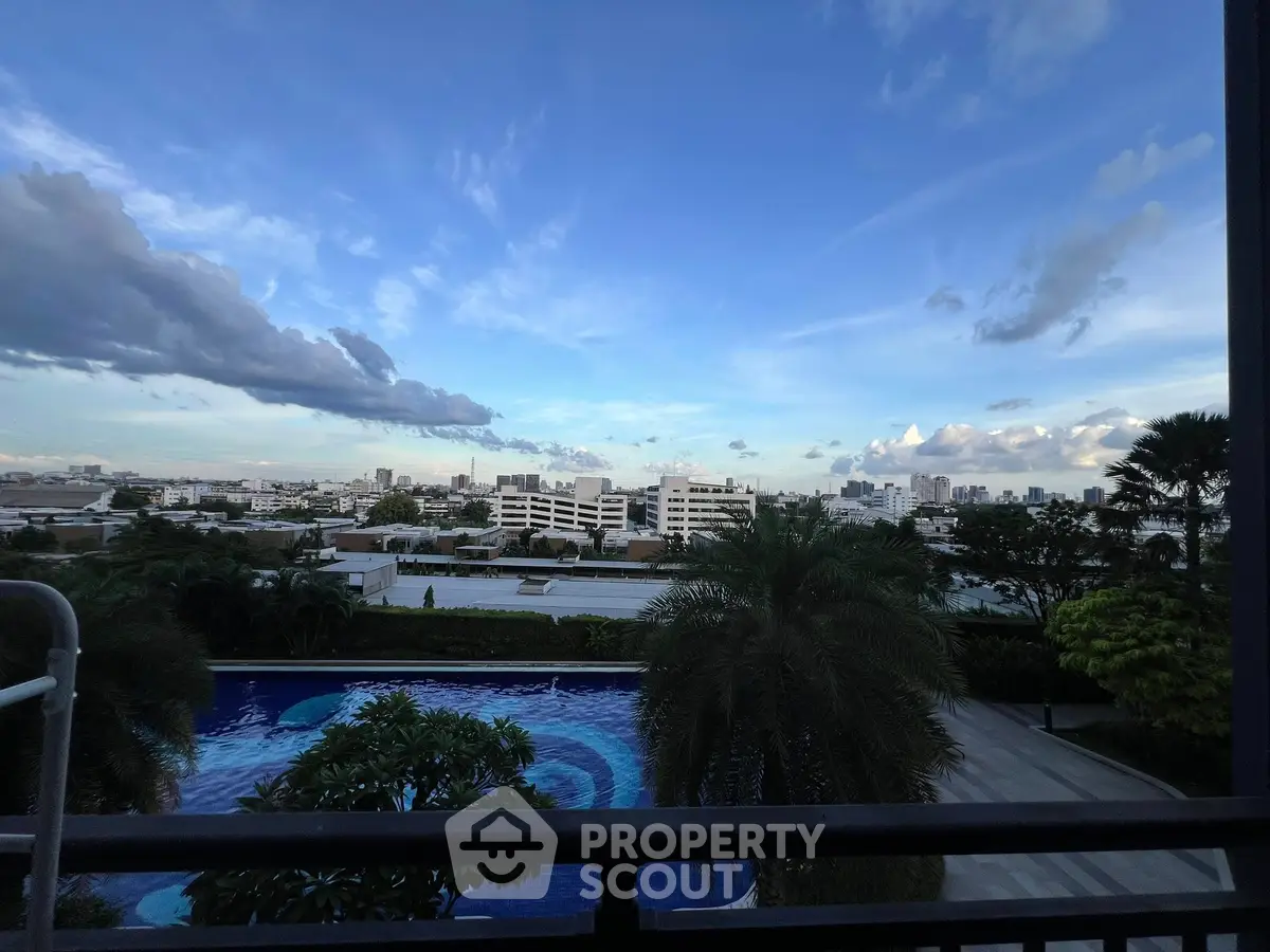 Stunning cityscape view from a balcony overlooking a luxurious pool and lush greenery.