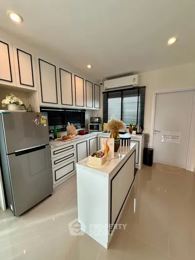 Modern kitchen with sleek cabinetry and island, featuring stainless steel fridge and stylish decor.