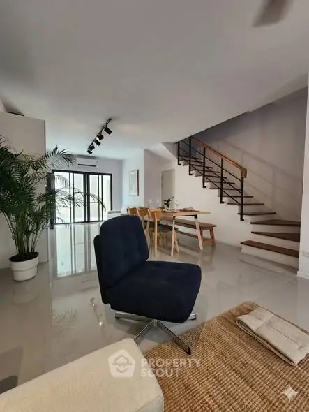 Modern living room with sleek staircase and dining area, featuring stylish furniture and natural light.