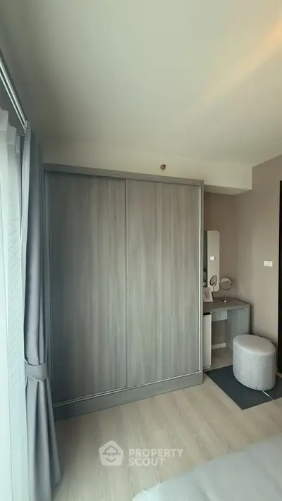Modern bedroom with sleek wardrobe and vanity area, featuring neutral tones and natural light.