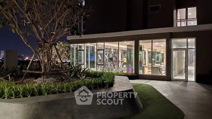 Modern gym with glass walls in a residential building at night, showcasing fitness amenities.