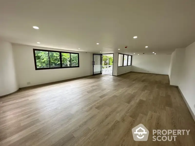 Spacious and well-lit living room with large windows offering a serene tree-lined view, perfect for a modern lifestyle.