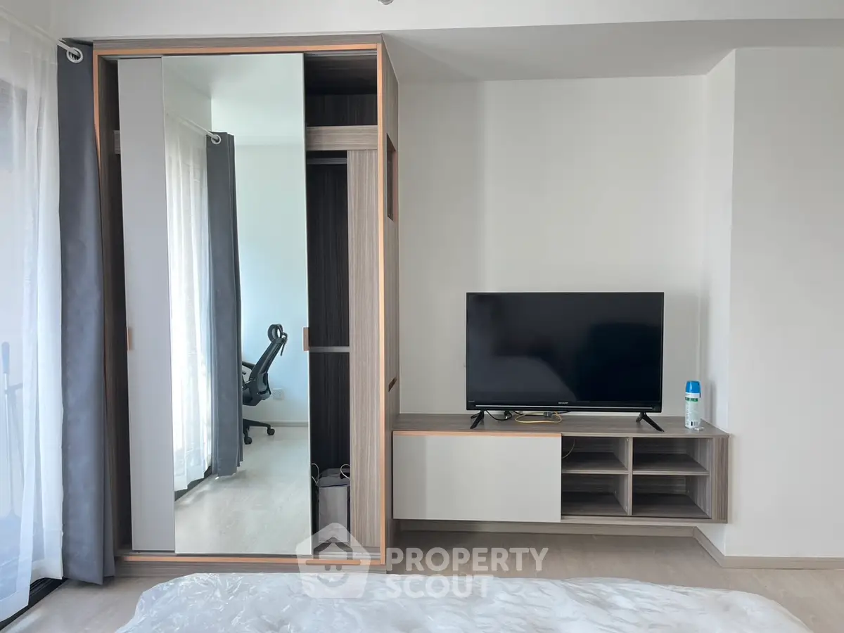 Modern bedroom with sleek wardrobe and TV unit, featuring a glimpse of a stylish study area.