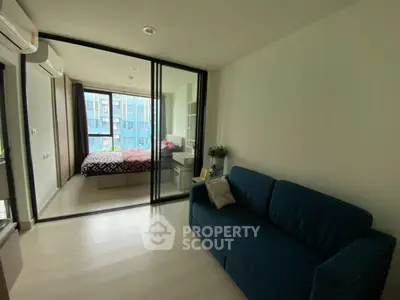 Modern apartment with glass partitioned bedroom and cozy living area, featuring a blue sofa and large windows.