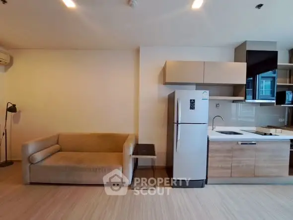 Modern open-layout living room with kitchen, featuring a cozy sofa and sleek appliances.