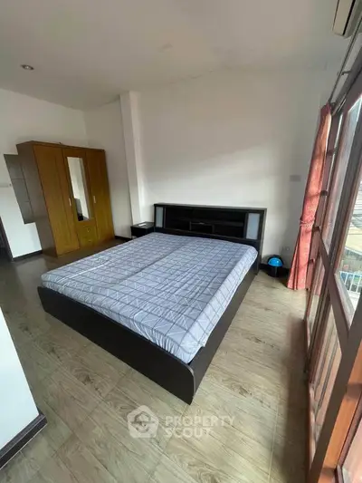 Spacious bedroom with wooden wardrobe and large window for natural light.