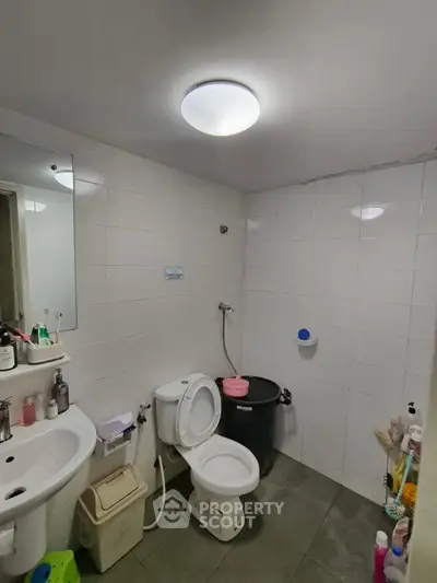 Modern bathroom with white tiles, toilet, sink, and ample storage space.