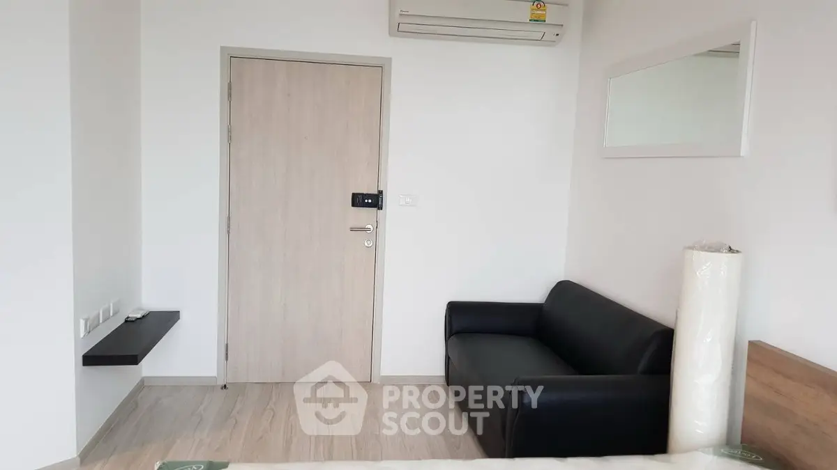 Modern minimalist living room with sleek black sofa and wall-mounted air conditioner.