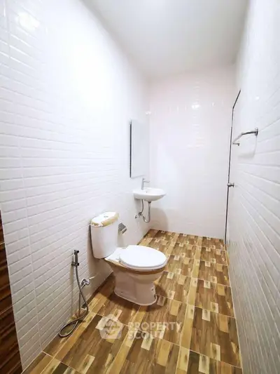 Modern bathroom with white tiled walls and wooden floor tiles, featuring a toilet and sink.