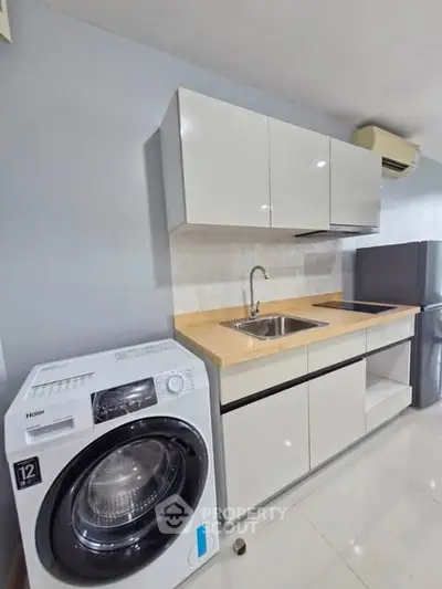 Modern kitchen with sleek cabinets, washing machine, and compact fridge in a stylish apartment.