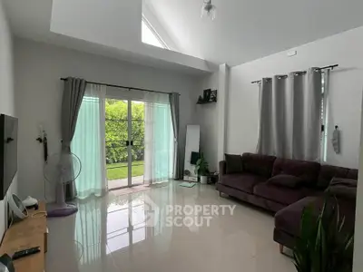 Spacious living room with high ceiling and garden view, featuring modern decor and natural light.