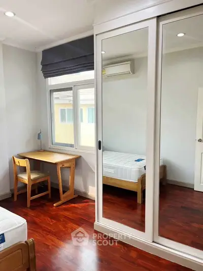 Bright bedroom with mirrored wardrobe and wooden flooring, featuring a cozy study corner.