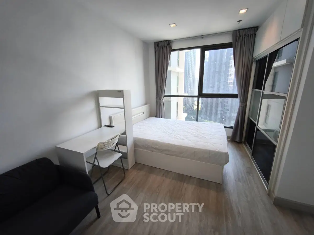 Modern bedroom with large window and city view, featuring sleek furniture and ample natural light.