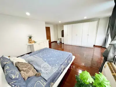 Spacious bedroom with elegant wooden flooring and ample natural light, featuring a cozy bed and large wardrobe.