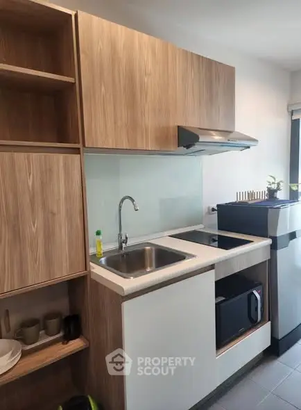 Modern compact kitchen with wooden cabinets and sleek appliances in a cozy apartment.