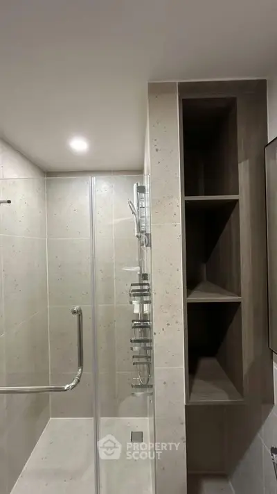 Modern bathroom with glass shower and built-in shelving, featuring sleek tile design.