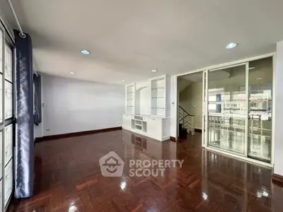Spacious living room with wooden flooring and built-in shelves, featuring large windows for natural light.