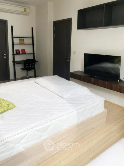 Modern bedroom with sleek furniture and wall-mounted TV, featuring a minimalist design and ample natural light.