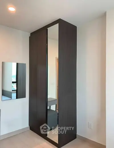 Modern bedroom with sleek dark wood wardrobe and mirror, minimalistic design, bright ambiance.