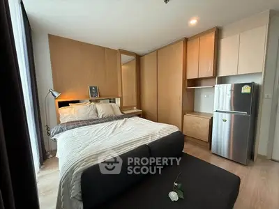 Modern bedroom with cozy bed, stylish lighting, and compact kitchen area in a sleek apartment.