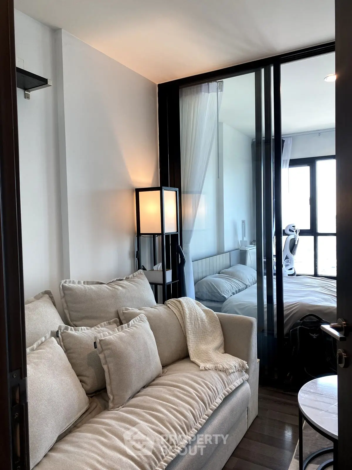 Modern living room with cozy sofa and glass partition leading to a stylish bedroom.