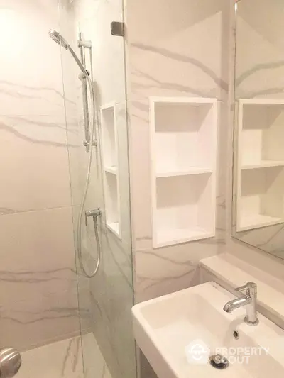 Elegant bathroom with marble tiles, glass shower enclosure, and built-in wall shelves, showcasing a modern and clean design.