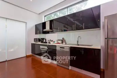 Modern kitchen with sleek black cabinets and stainless steel appliances, featuring a large window for natural light.