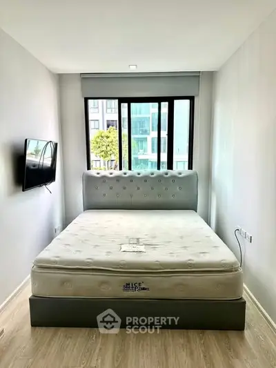 Modern bedroom with large window and wall-mounted TV in a stylish apartment.