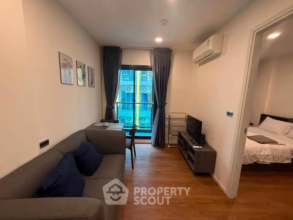 Modern living room with cozy sofa and TV, adjacent to a bedroom, featuring wooden flooring and balcony view.