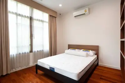 Bright bedroom with wooden flooring and large window, featuring a modern air conditioning unit.