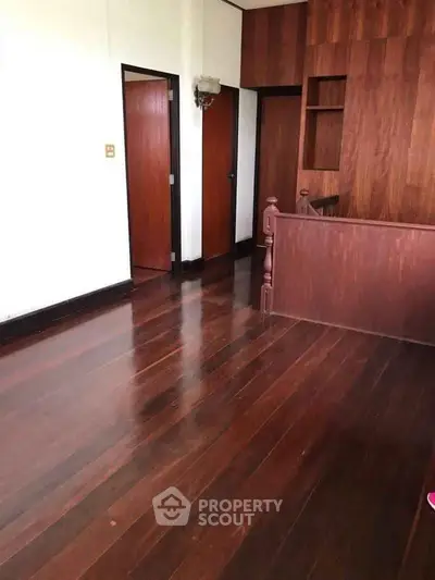 Spacious wooden-floored room with elegant wood paneling and built-in shelving, perfect for customization.