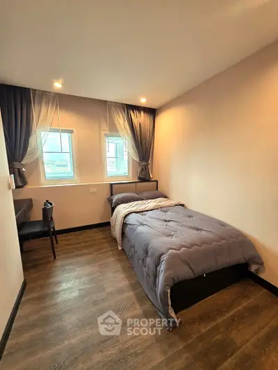Cozy bedroom with single bed, wooden flooring, and natural light from two windows.