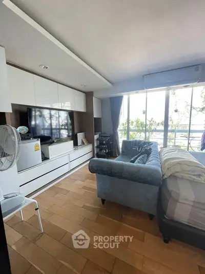 Spacious living room with large TV and cozy sofa, featuring a bright window view.