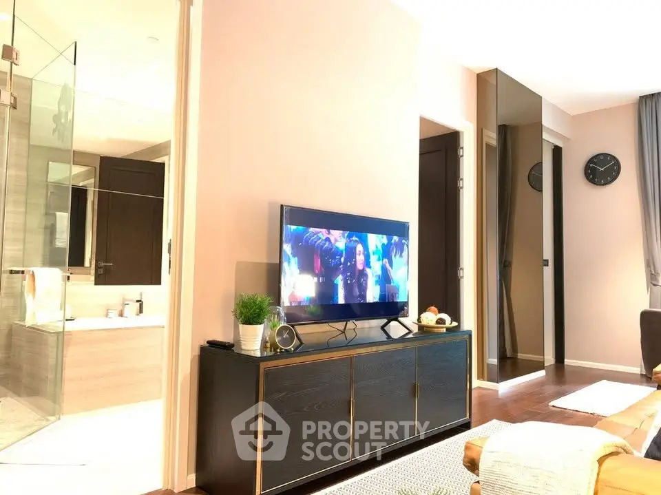 Modern living room with TV and stylish decor adjacent to a bathroom with glass shower.