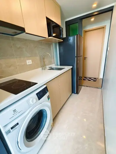 Modern kitchen with sleek appliances and compact design, featuring a washing machine and fridge.