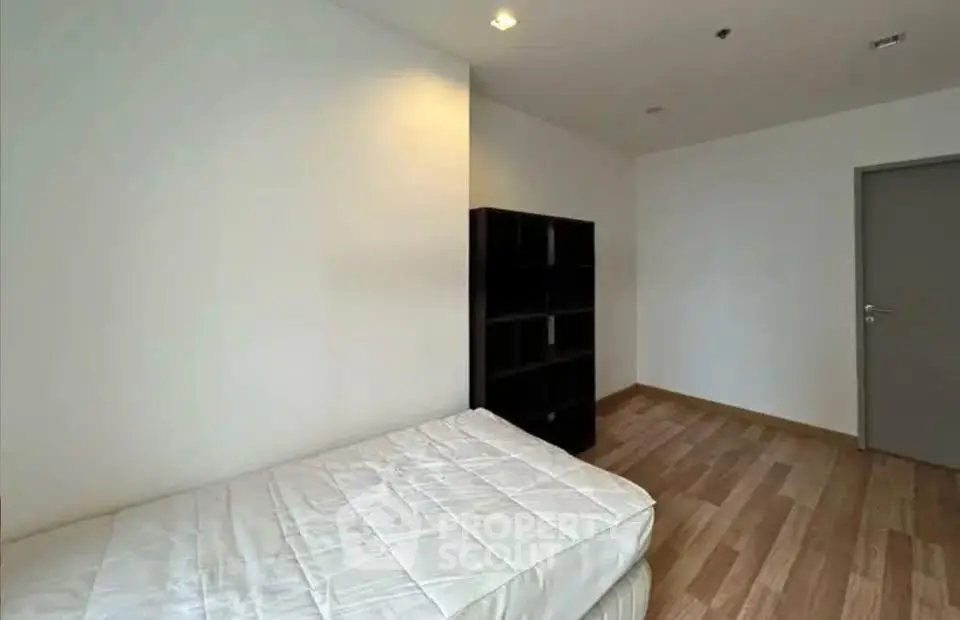Minimalist bedroom with wooden flooring and a simple bed setup.