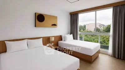 Modern bedroom with two beds and large window offering lush green view.
