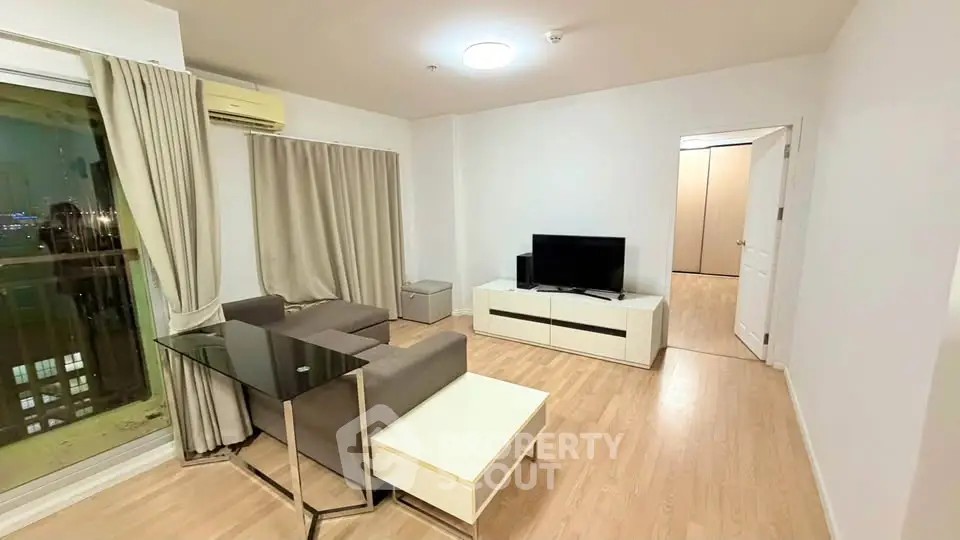 Modern living room with sleek furniture and large window offering city views.
