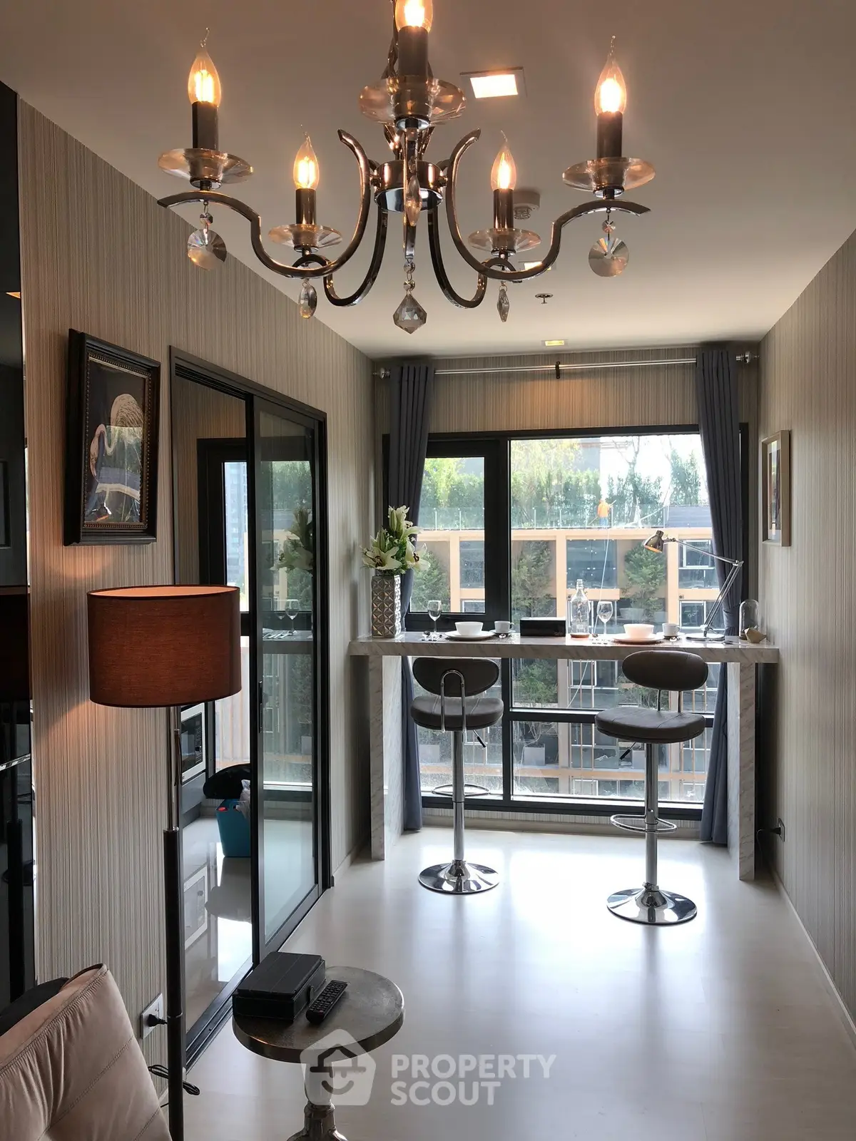 Modern living room with elegant chandelier and balcony view, featuring stylish bar stools and large windows.