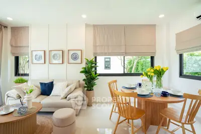 Bright and modern living room with stylish decor and dining area, featuring large windows and lush greenery.