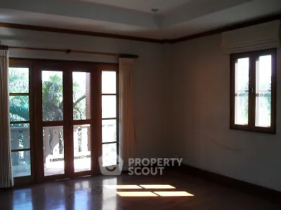 Spacious room with wooden floors and large windows offering natural light and garden view.