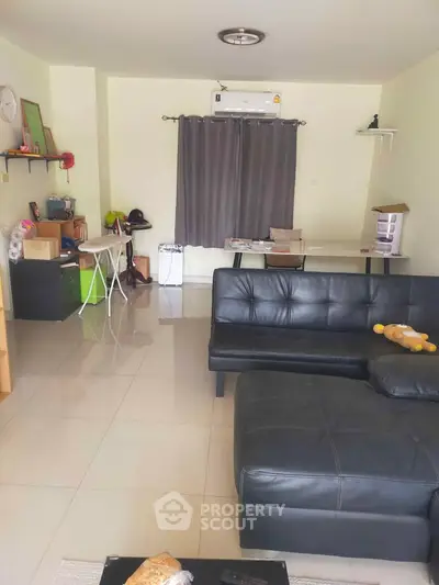 Spacious living room with modern black leather sofa and sleek tile flooring.