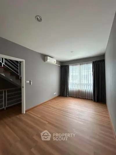 Spacious empty room with wooden flooring and large window, perfect for customization.