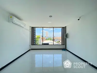 Bright and airy corner unit with expansive windows offering a city view, glossy tiled floors, and a modern air conditioning unit, perfect for a comfortable urban living space.